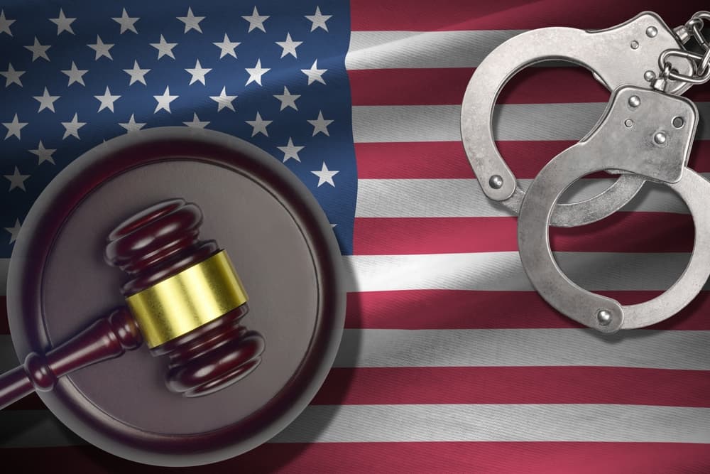 United States flag with a judge's gavel and handcuffs in a dimly lit room. A concept image representing crime, justice, and punishment, suitable for discussions on guilt and legal consequences.