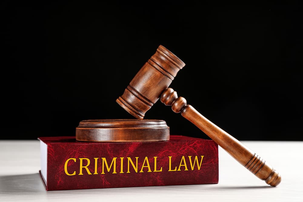 A judge's gavel rests on a book atop a white table, set against a black background, symbolizing the concept of criminal law.